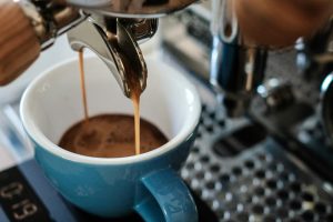 Two streams of golden espresso flowing from a chrome portafilter into a blue ceramic cup.