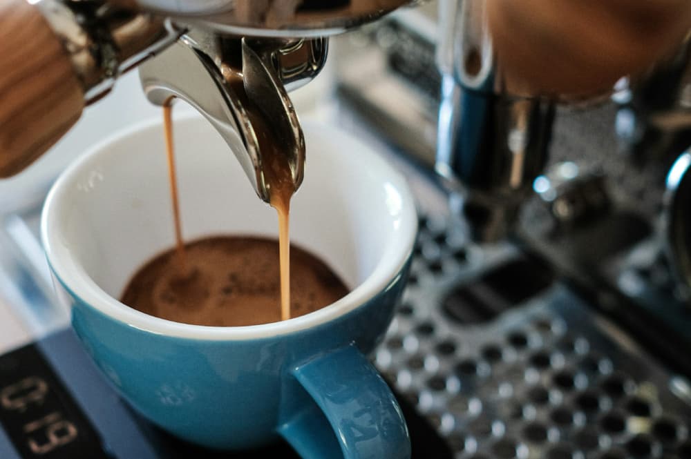 Two streams of golden espresso flowing from a chrome portafilter into a blue ceramic cup.